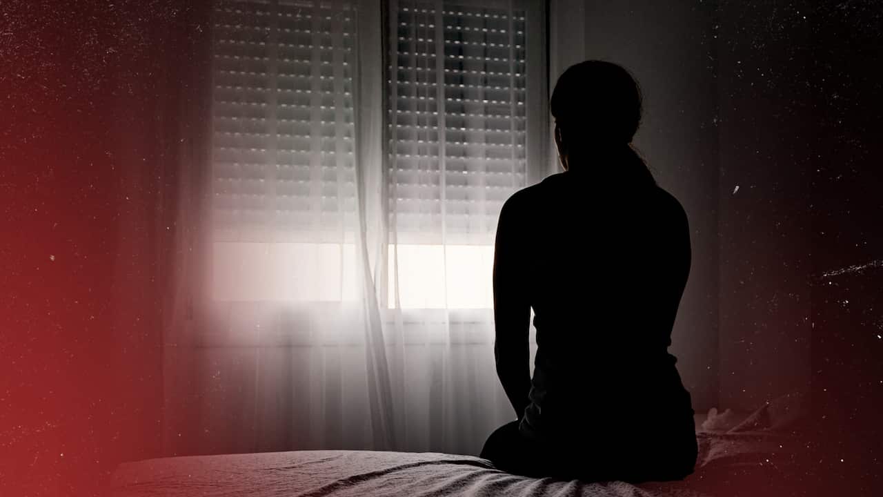 An unidentified woman sits on a bed looking out of the window.