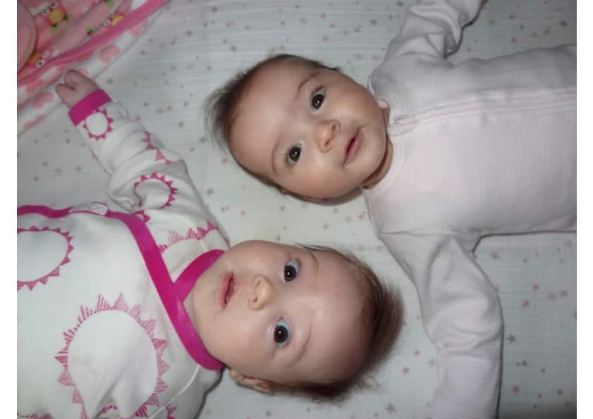 An image of two alert, happy and health babies, lying on their backs in bodysuits.