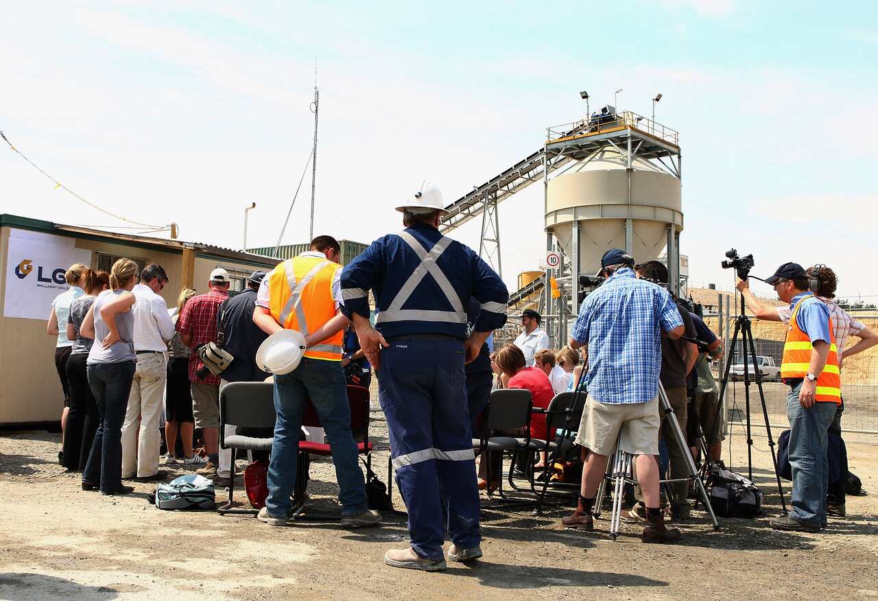 A group of people gather around, some in high viz gear and helmets, others with camera gear.