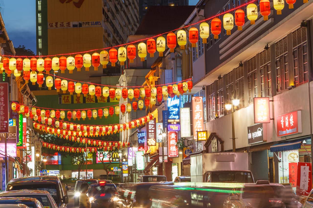 Yellow and red lanterns strung up above a busy street with neon signs along the buildings. 