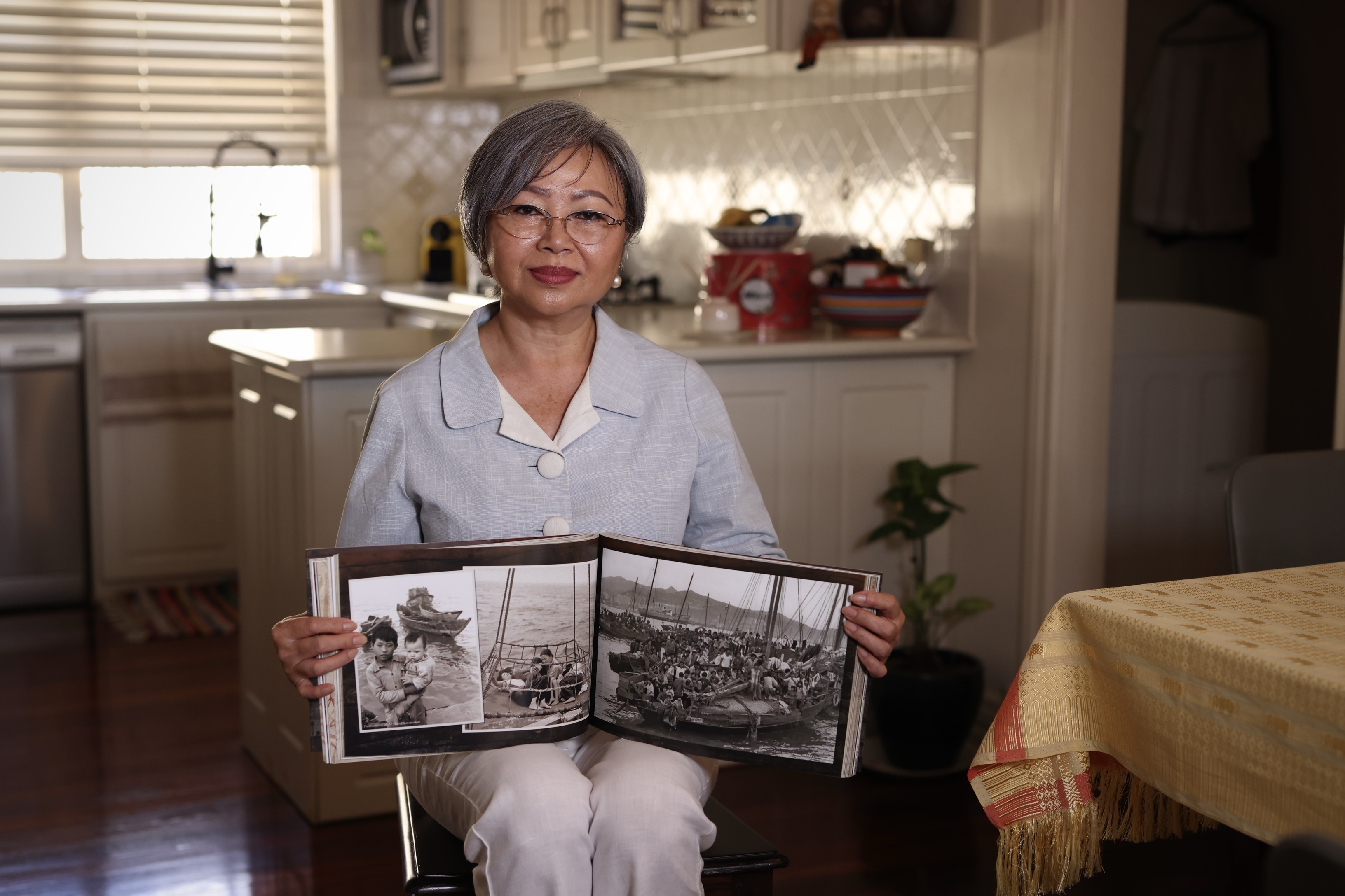 A woman showing photos inside a book, as she sits on a chair.