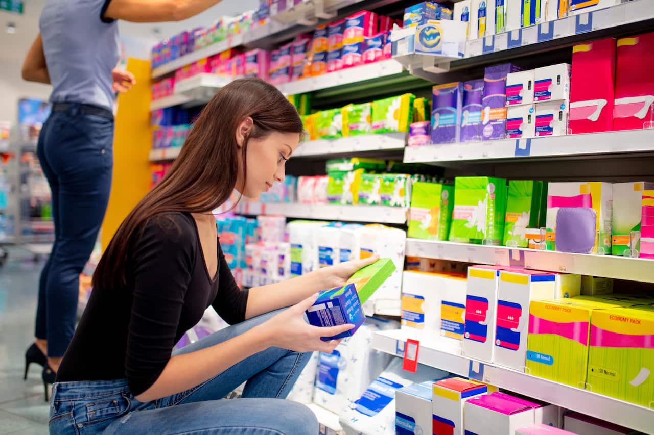 A woman crouching and choosing sanitary pads. Another woman standing in the background.