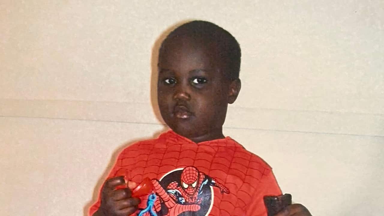 A young boy with a focused expression wears a red Spider-Man hooded shirt while holding small toys.