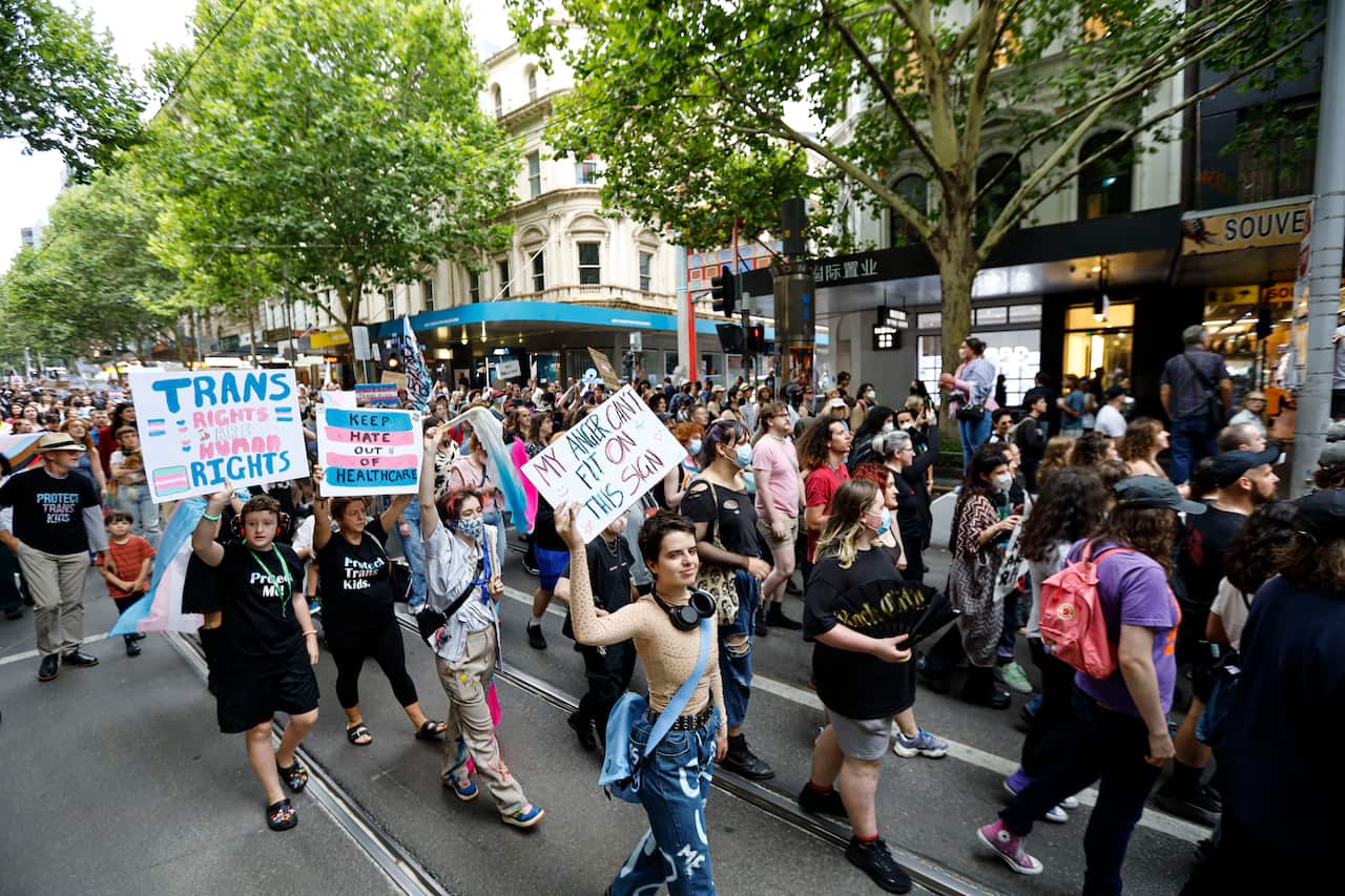 Protesters walk on a busy street, with some holding placards. 