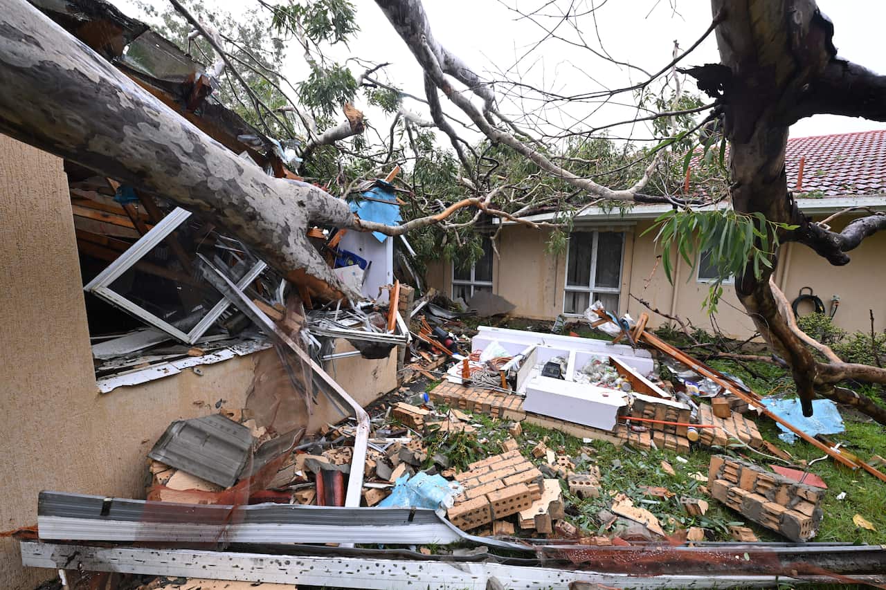 An uprooted tree crashed into a house with debris scattered around