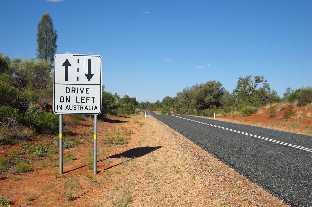 A sign by a remote road that reads 'Drive on left in Australia'