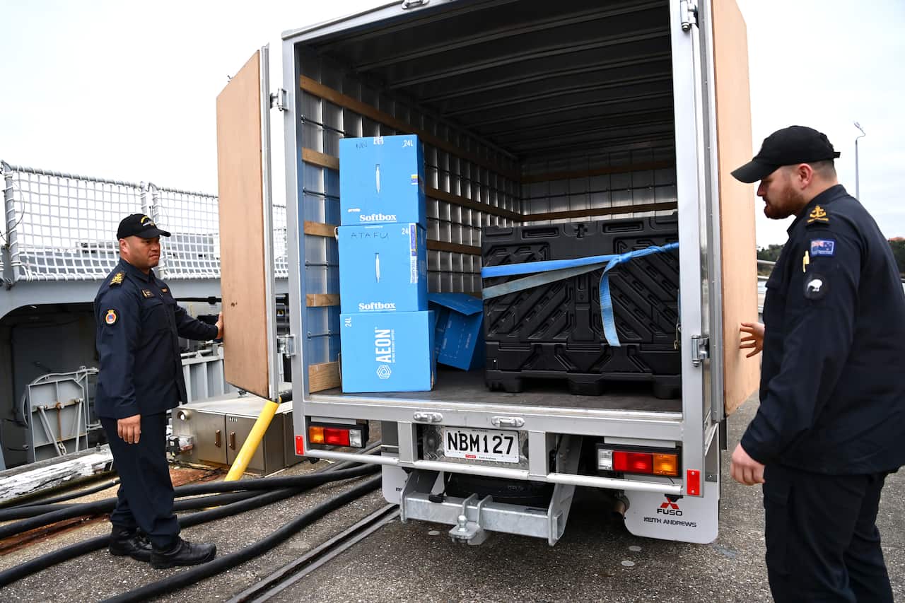 Two man in uniform loading a truck with blue boxes.