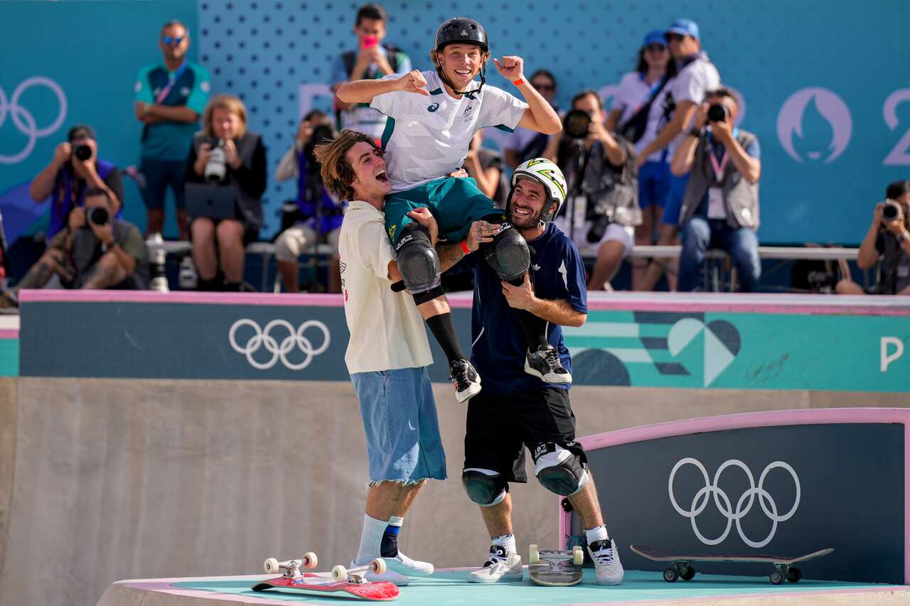Two men lift another man on their shoulders in a skatepark. There are two skateboards near them on the ground
