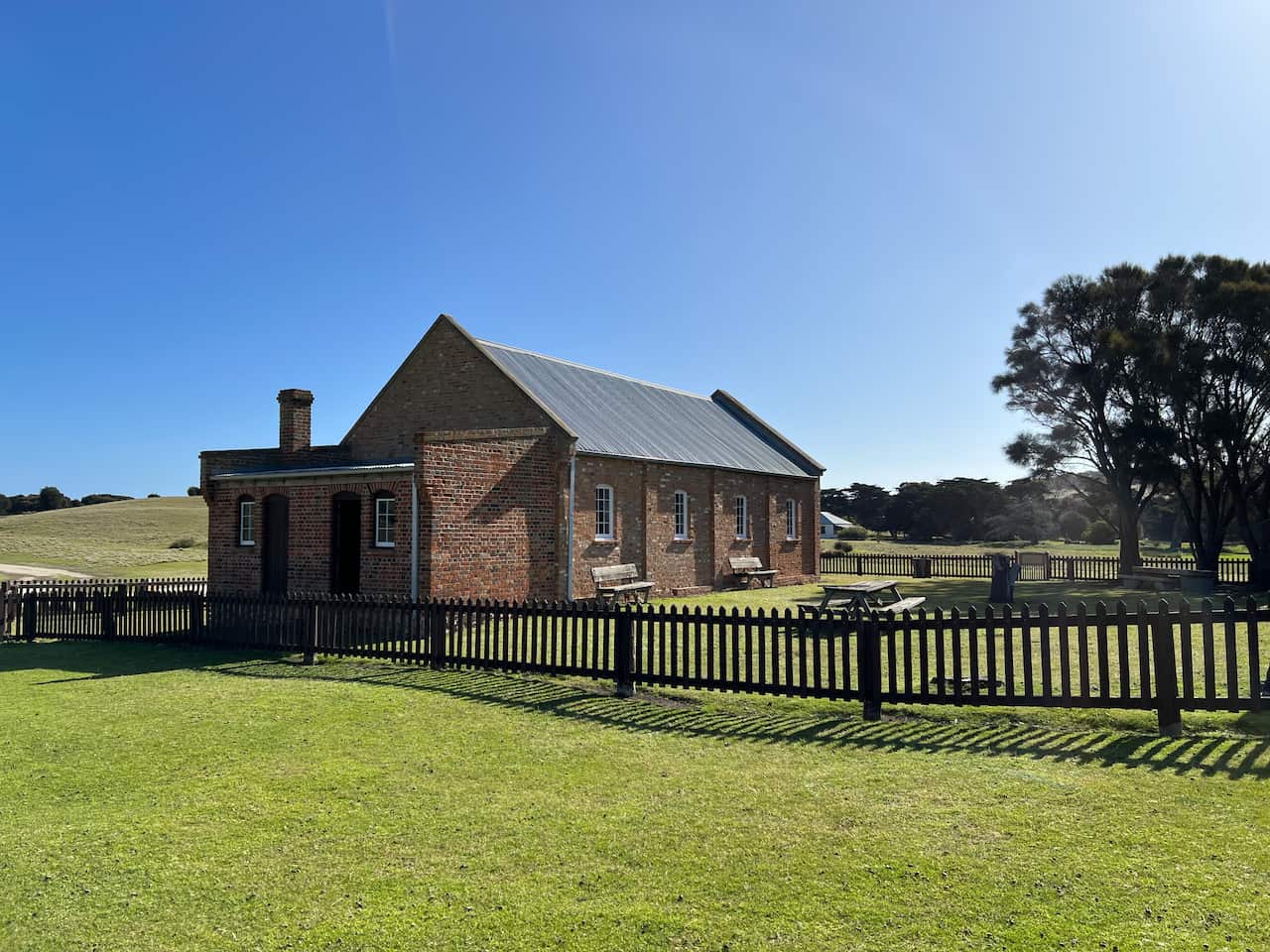A brick chapel sits inside a picket fence with manicured lawns all around.
