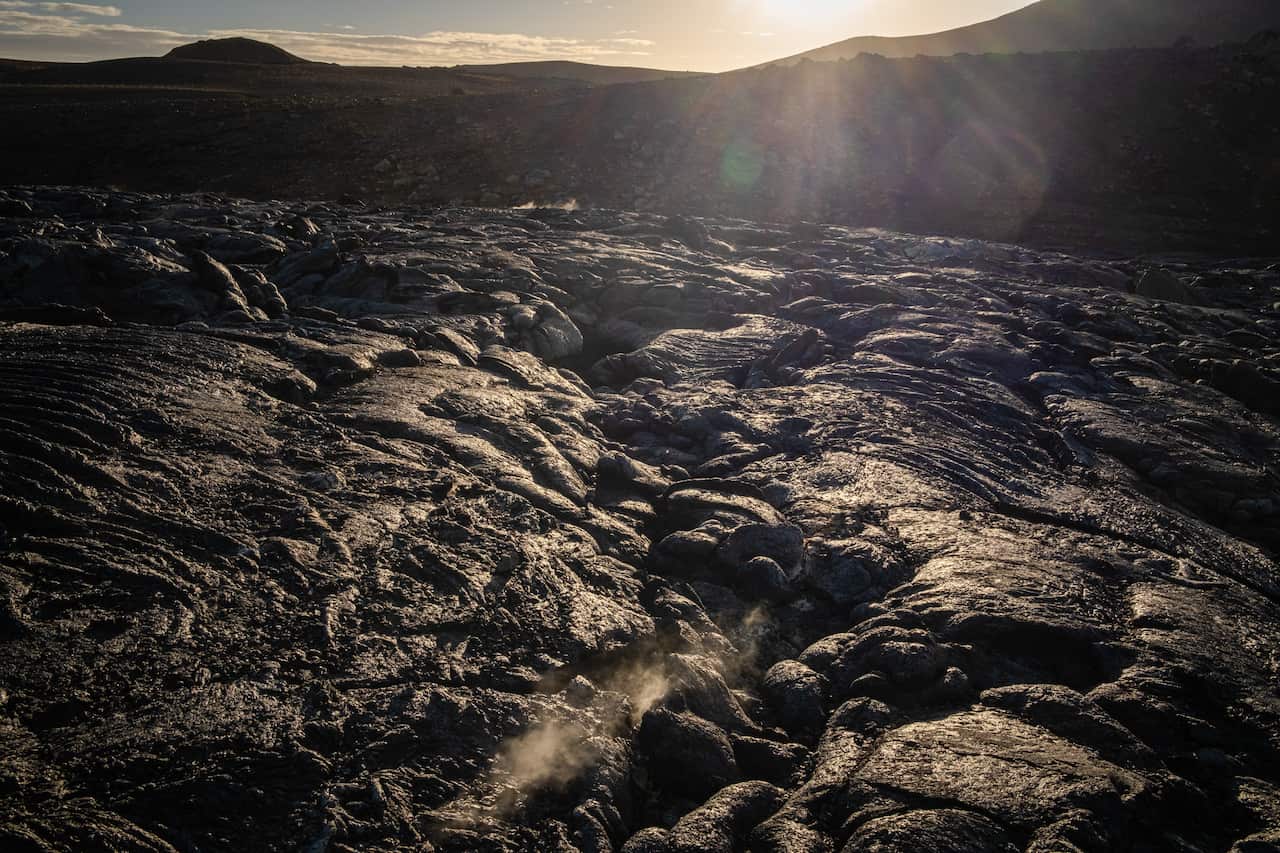 A lava field fringed by dark hills in what looks like either early morning or late afternoon light.