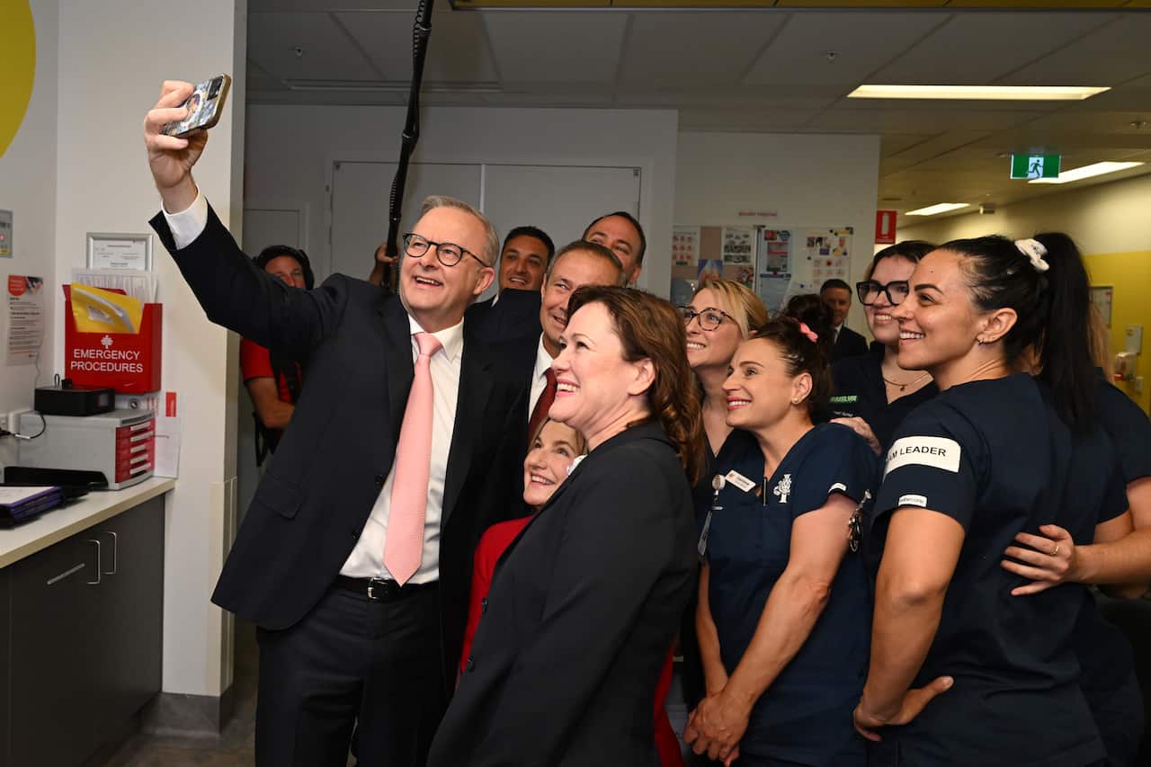 Anthony Albanese holds up a phone, taking a selfie with a group of people.