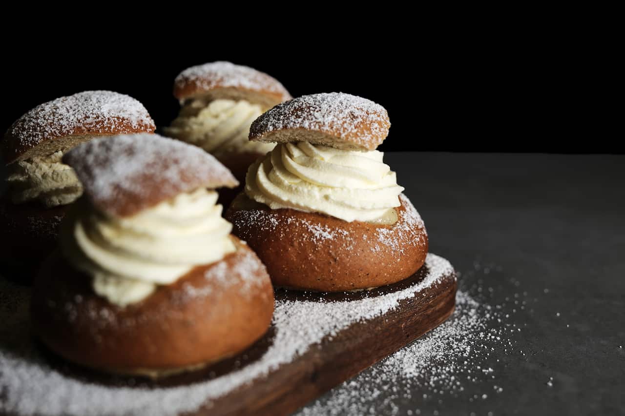 Pastries filled with whipped cream and sprinkled with icing sugar on a wooden board.
