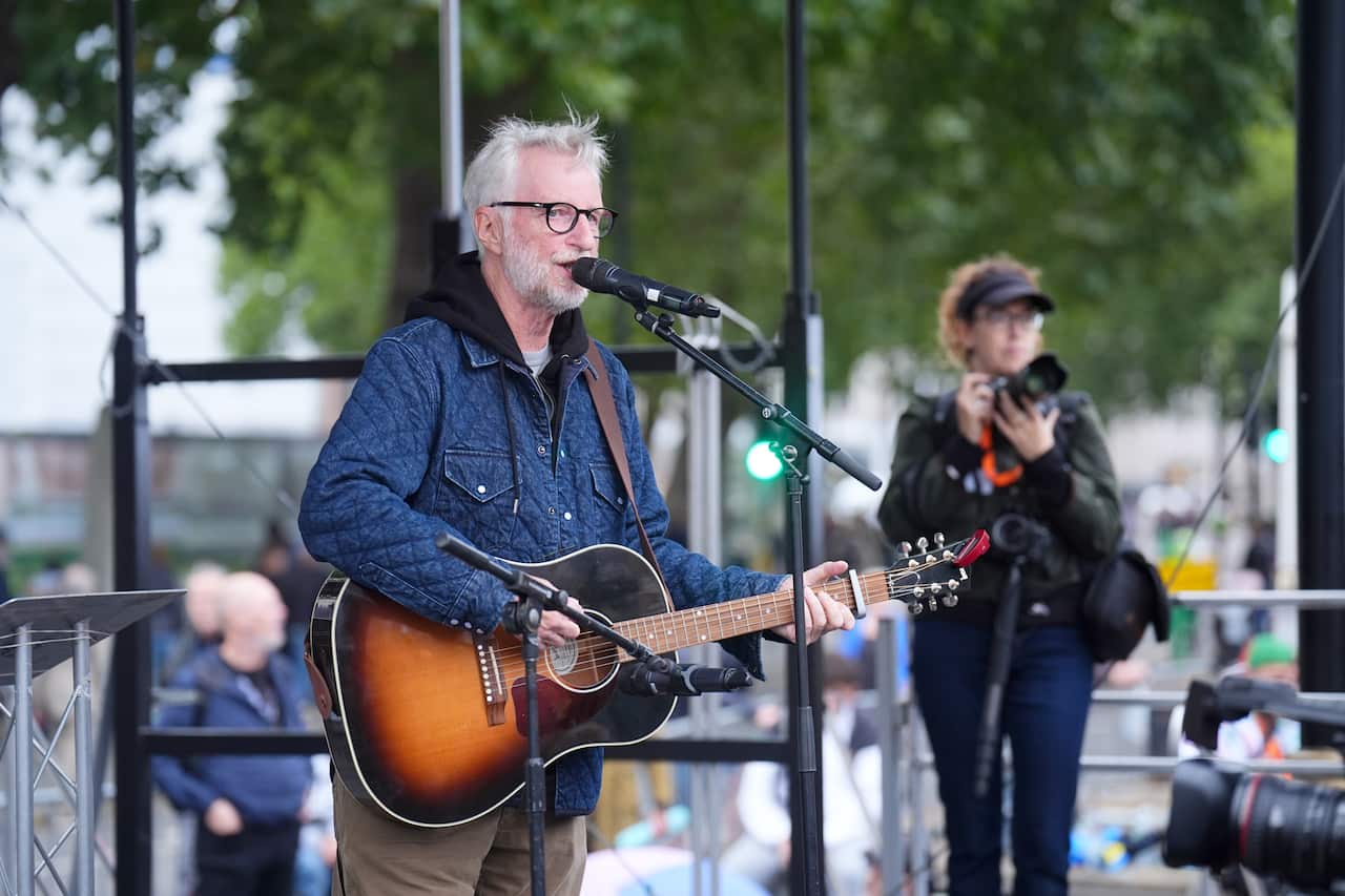 A man wearing a blue coat plays guitar and sings into a microphone.