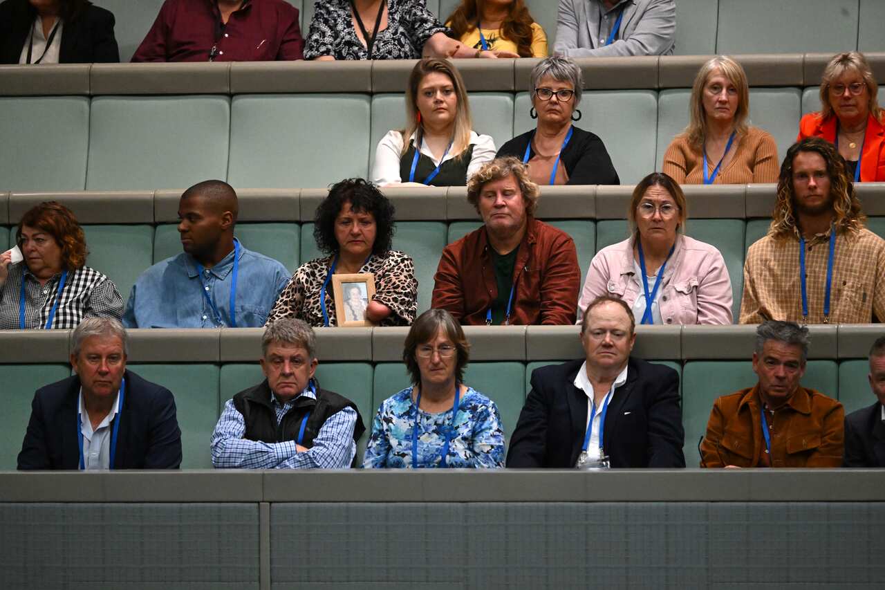 Rows of people listen to a speech, as one woman holds a picture. 