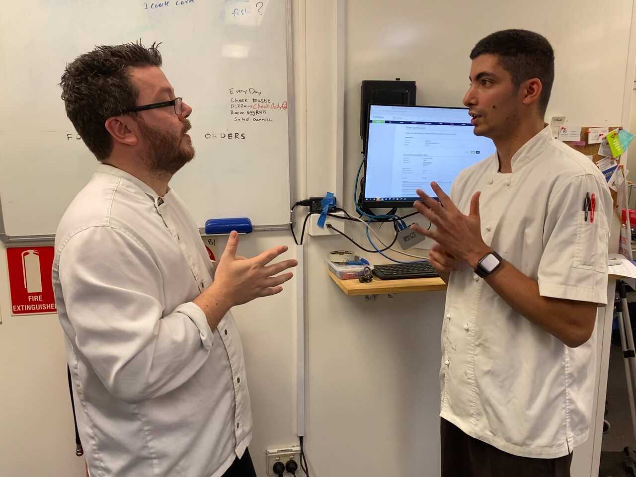Two men in a kitchen communicate with each other using Auslan