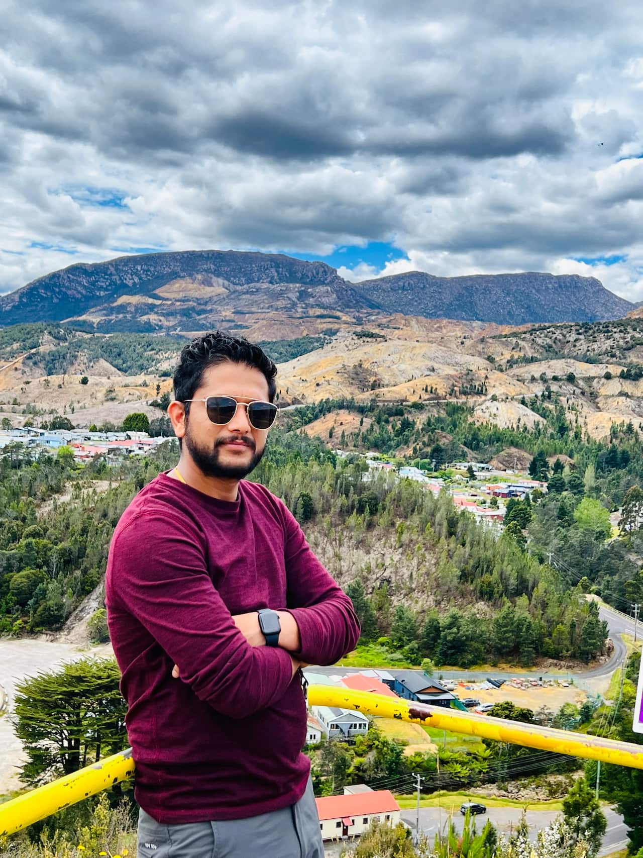A man standing on a lookout with hilly country in the background.