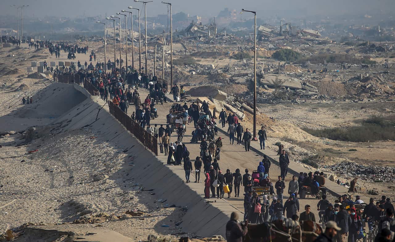 A large crowd of people walk down a road surrounded by destroyed buildings