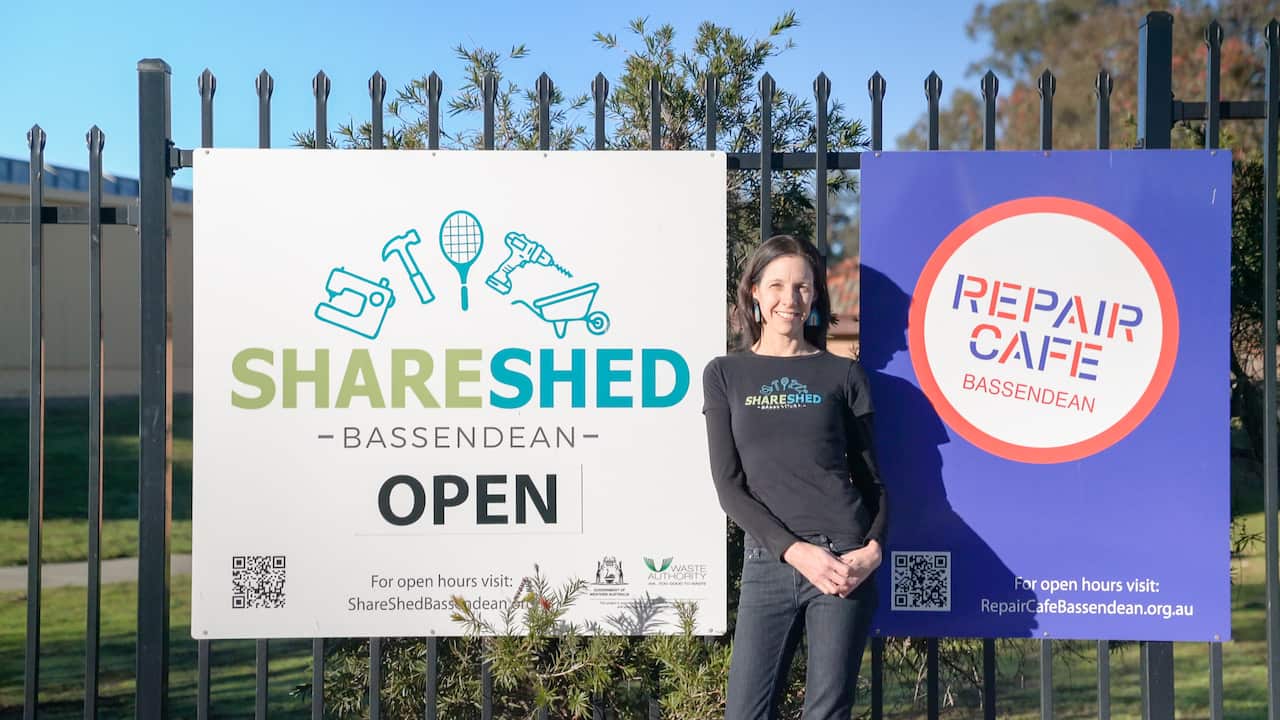 Renée McLennan standing in between signs for the Share Shed and the local repair cafe.