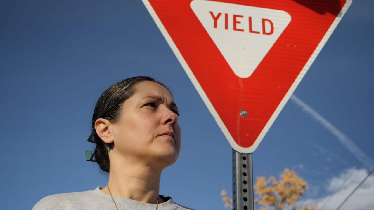 A woman stands in front of a road sign which says 'yield'. 