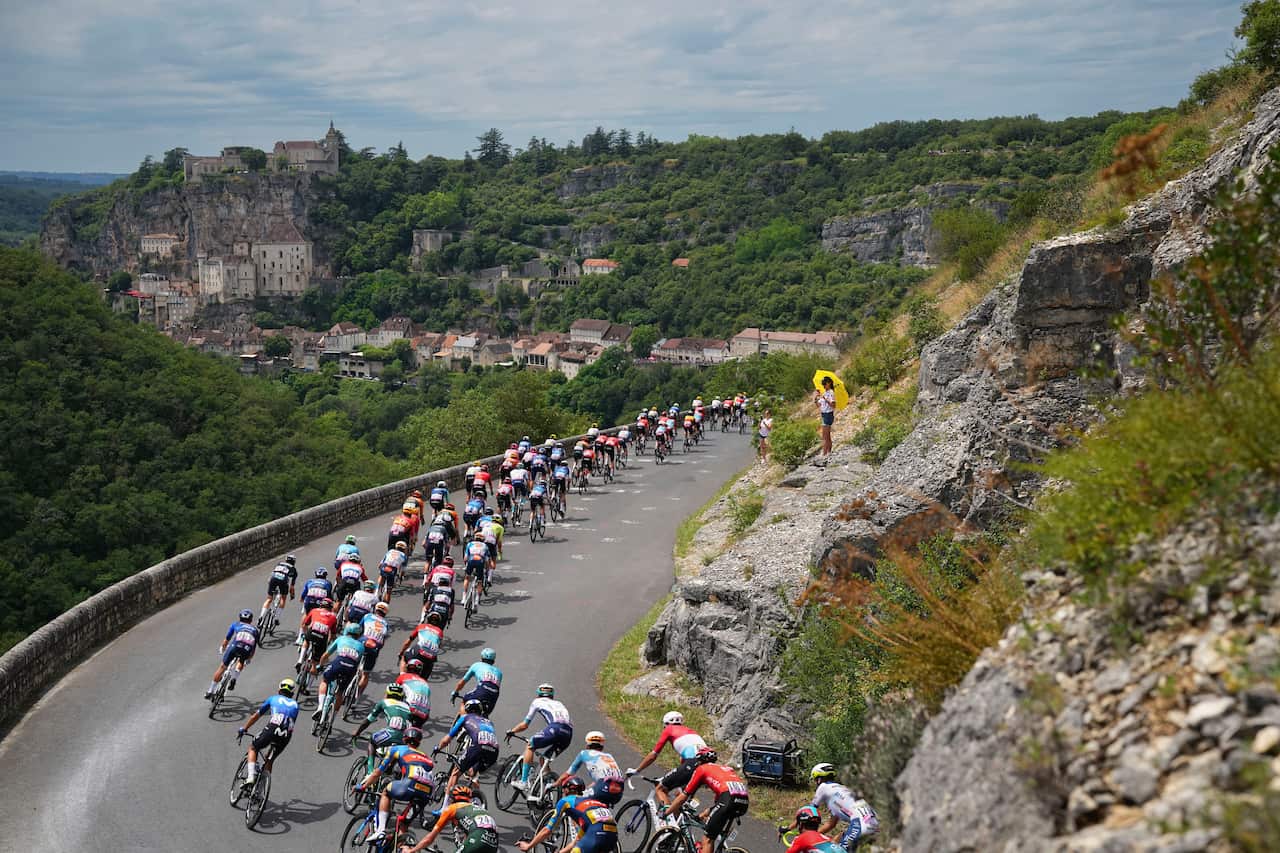 A large pack of cyclists descends a hill.