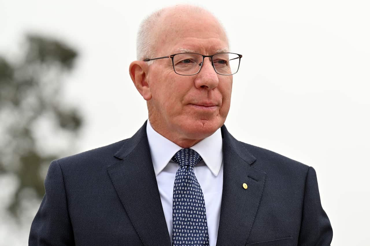 A man wearing a suit, tie and glasses standing outside.