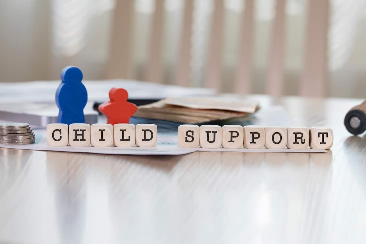 Two wooden figures, one blue and one red, stand beside wooden letters spelling "child support".