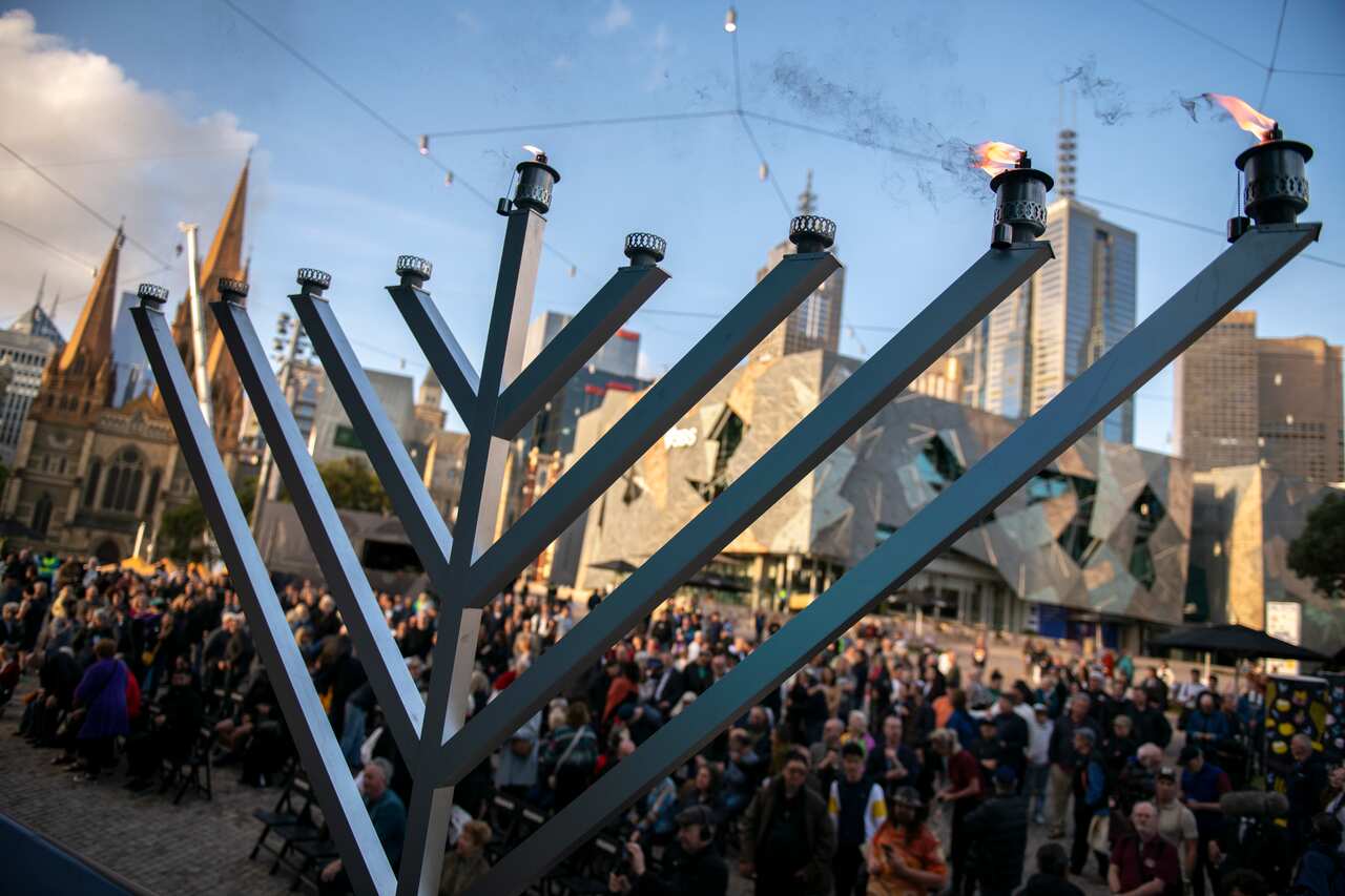 A menorah stands with 3 candles burning during a Chanukah - Pillars of Light public event