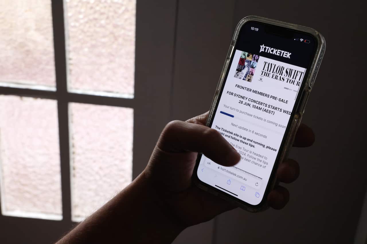 A hand holding a phone showing a virtual queue for Taylor Swift tickets.