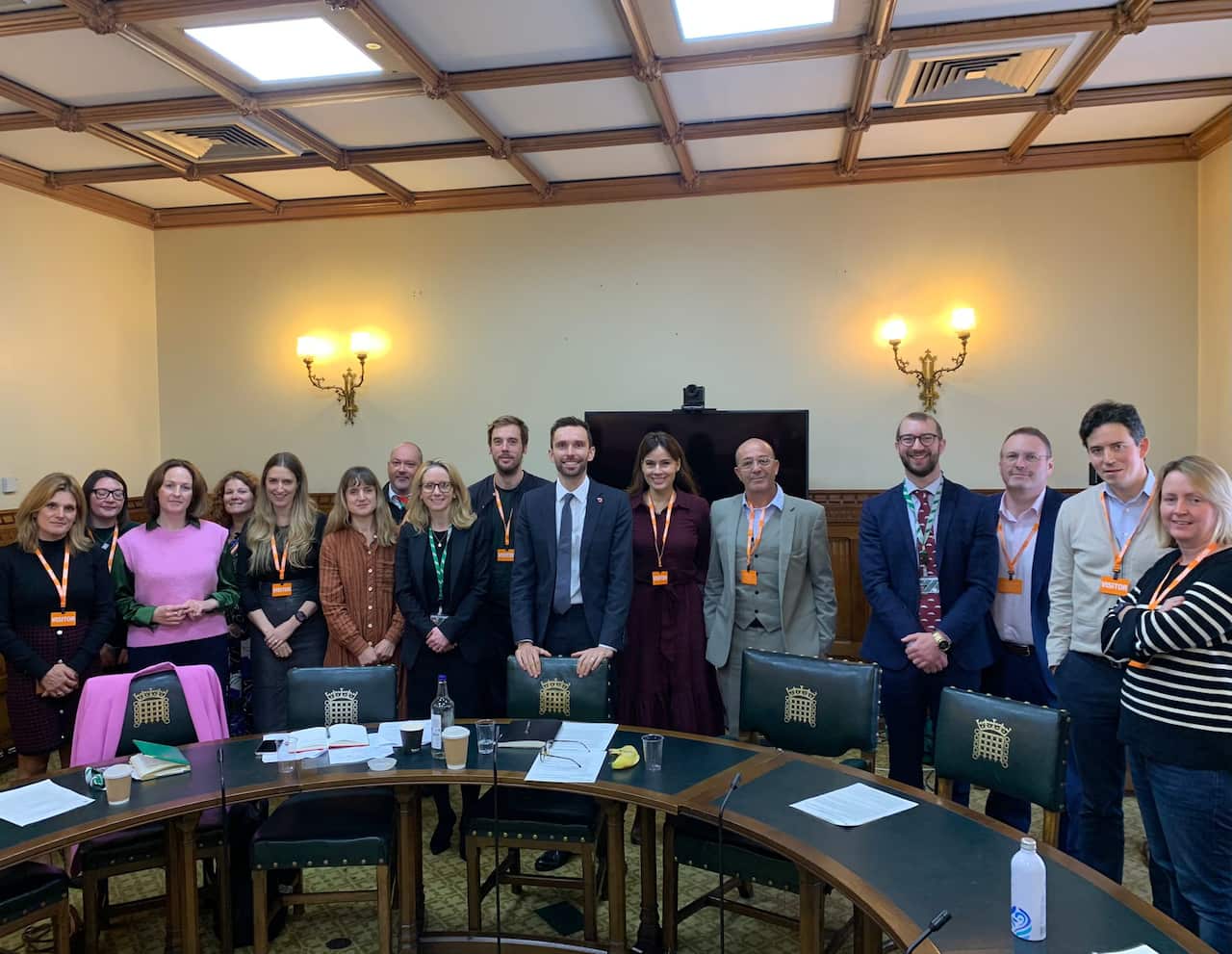 A group of politicians and SFC founders stand before green chairs of a committee room. 