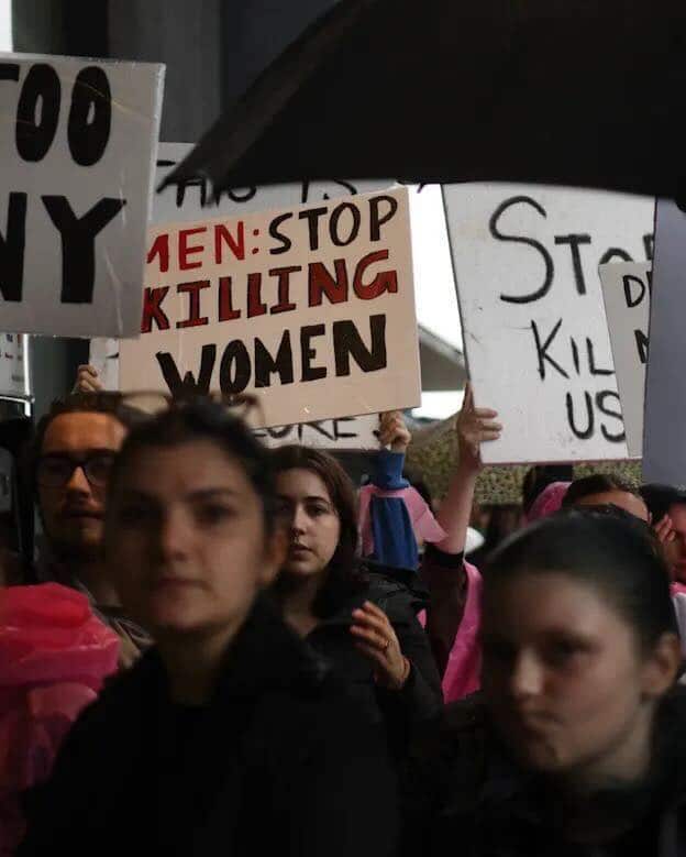 A group of people marching, some holding up signs about violence against women.