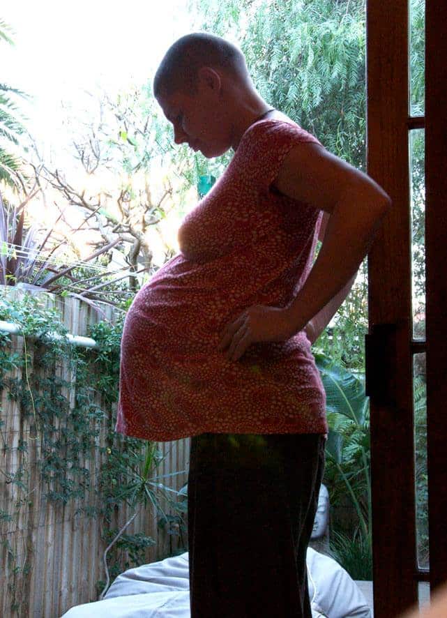 A pregnant woman with a shaved head looks down at her unborn child.
