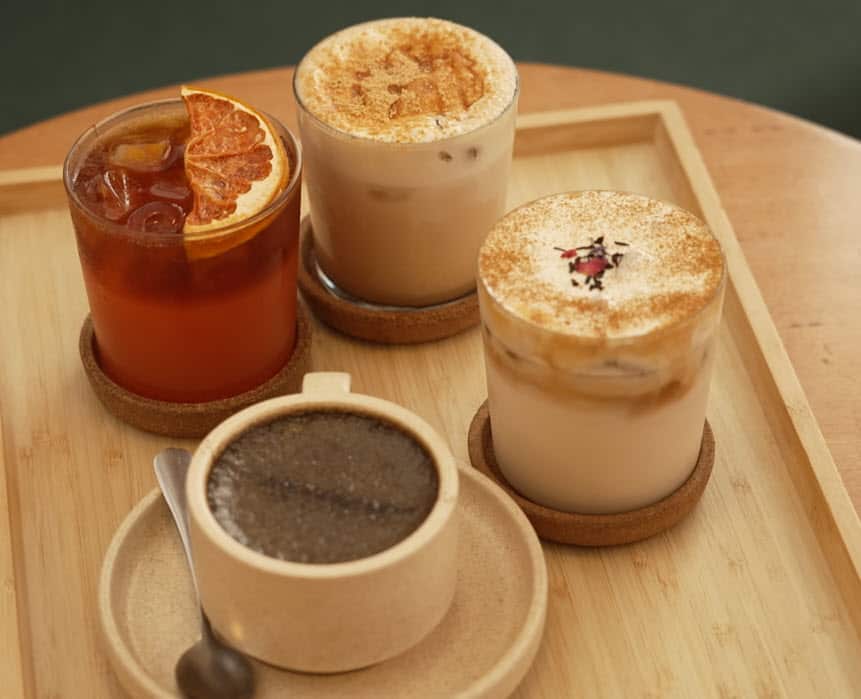Four drinks sit on a  tray, traditional coffee in a cup, two creamy styles and a fruit based drink.