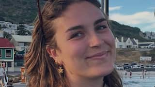 a closeup photo of a young woman smiling in front of a Scandinavian coastal town