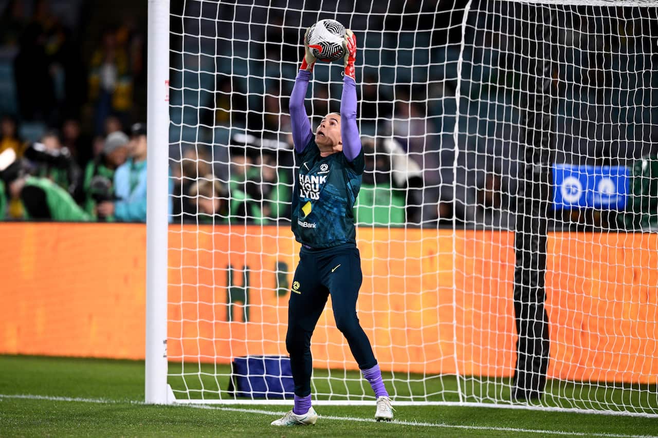 Goalkeeper Lydia Williams in the Matilda's kit, grabbing a ball from above her head standing inside the net.