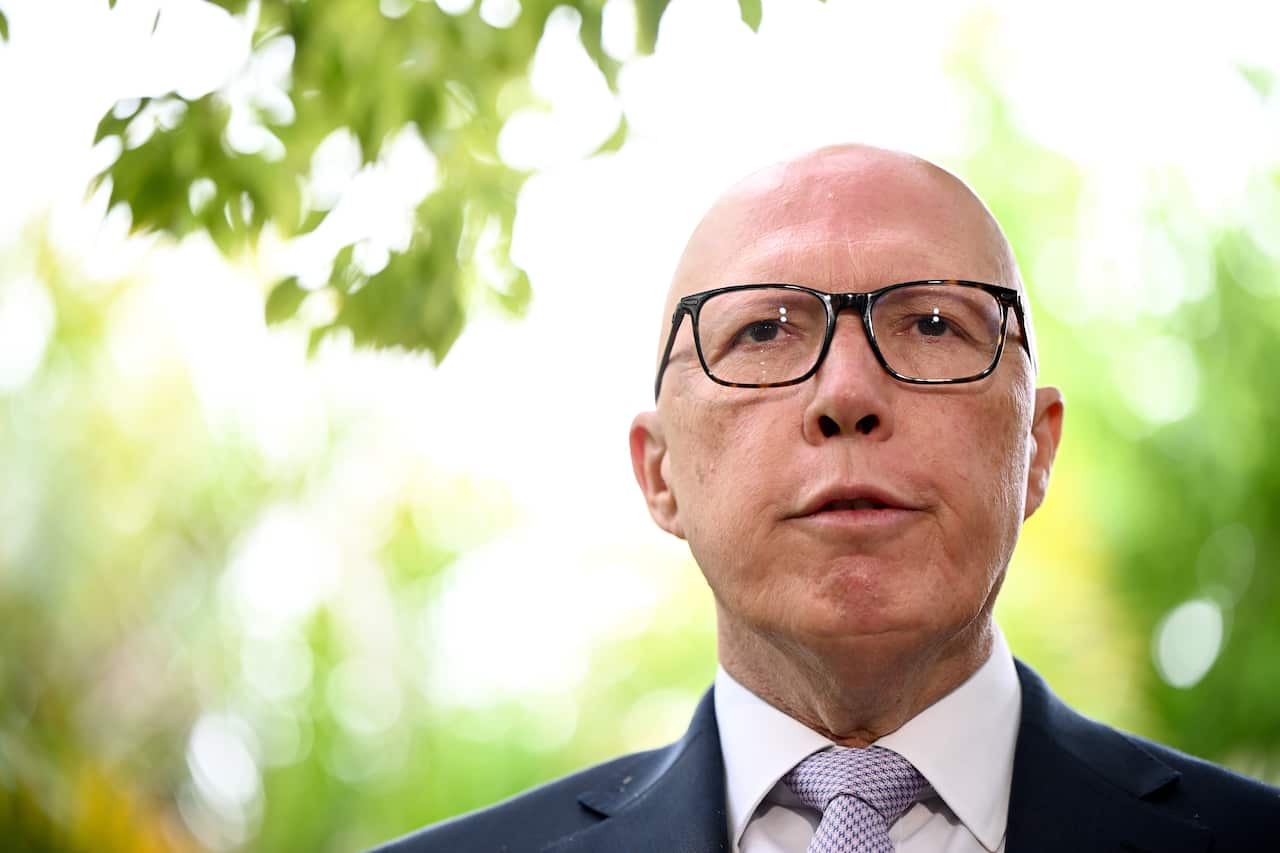 Peter Dutton standing in front of green trees.