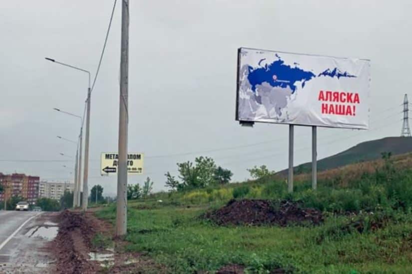 A billboard on a green patch by the roadside reads 'Alaska is ours' in Russian.