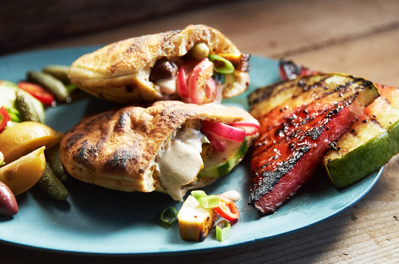 Two filled pitas sit on a round blue plate, alonside wedges of watermelon with char marks. 