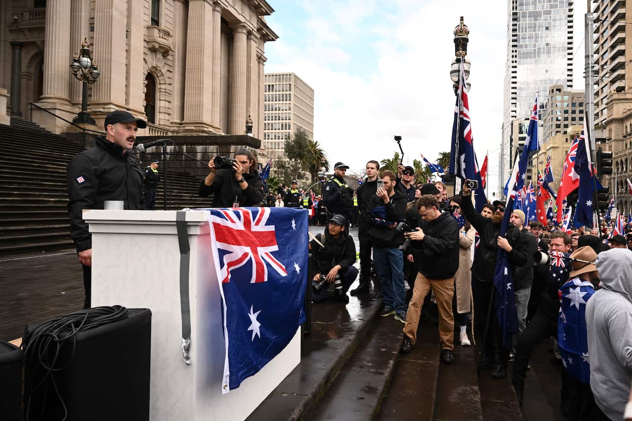 A man addresses a crowd waving Australian flags. 