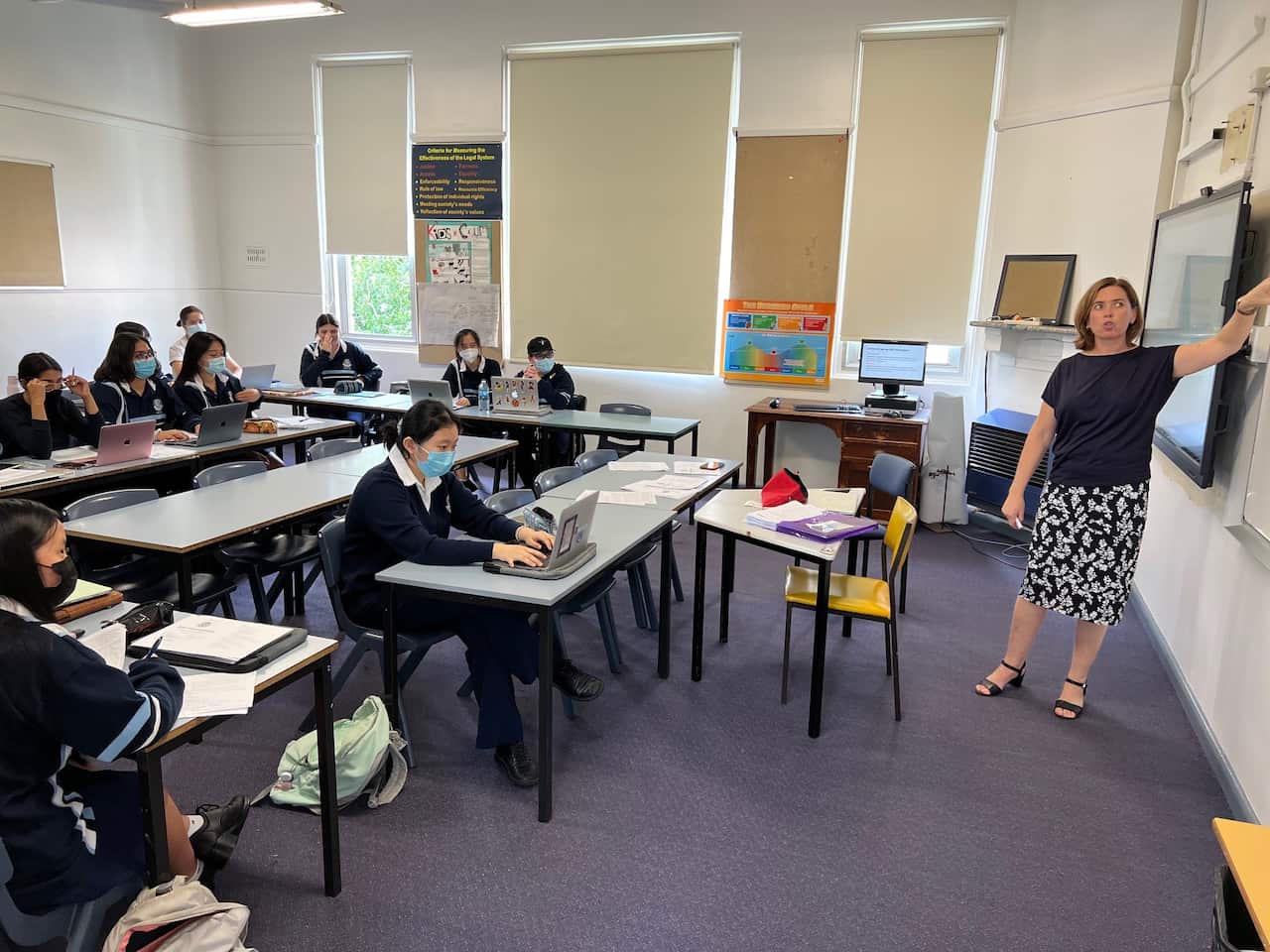 Teacher pointing to whiteboard in school classroom as students at desks look on.