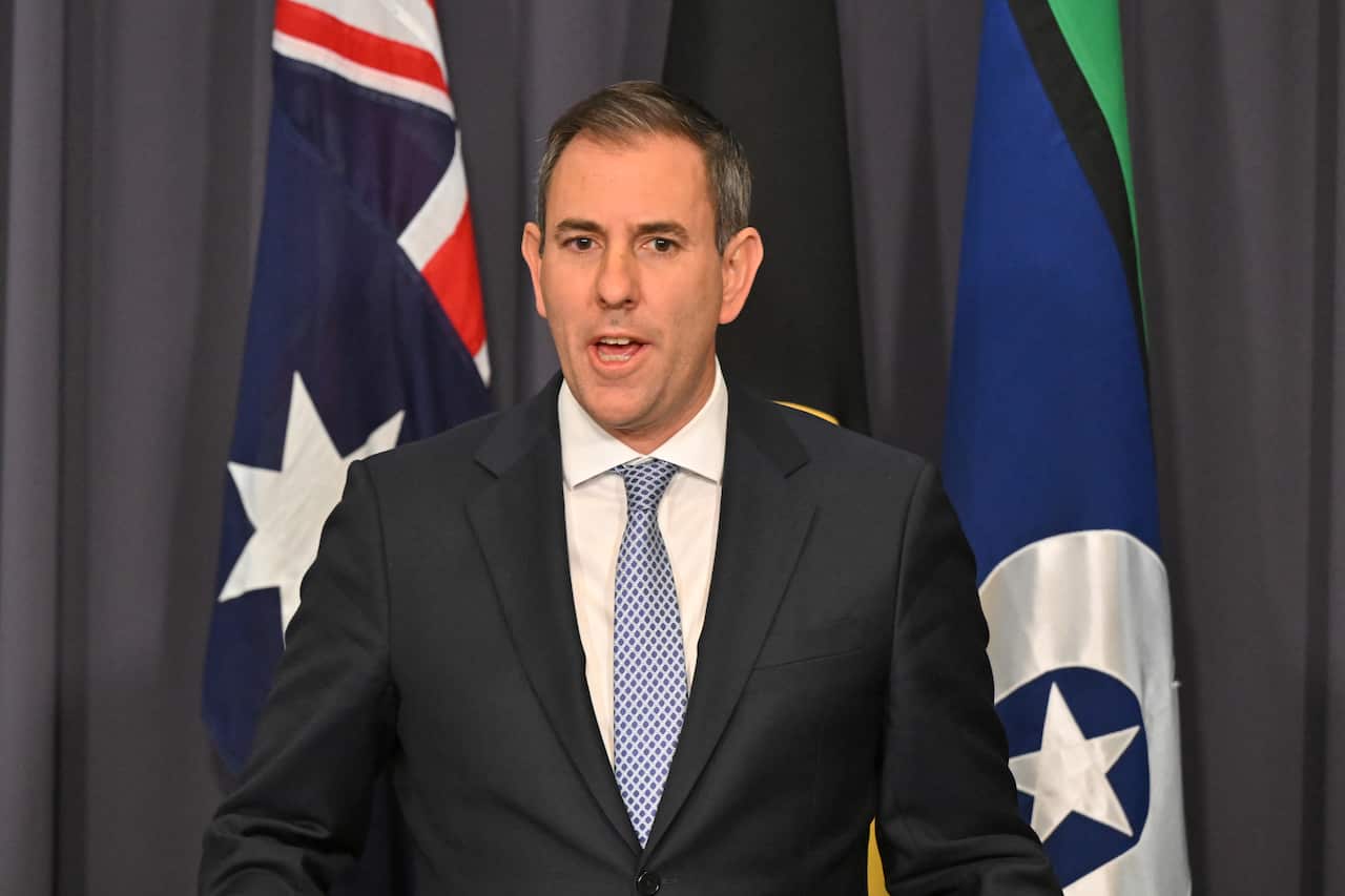 A man speaking at a podium, standing in front of Australian, Aboriginal and Torres Strait Islander flags.