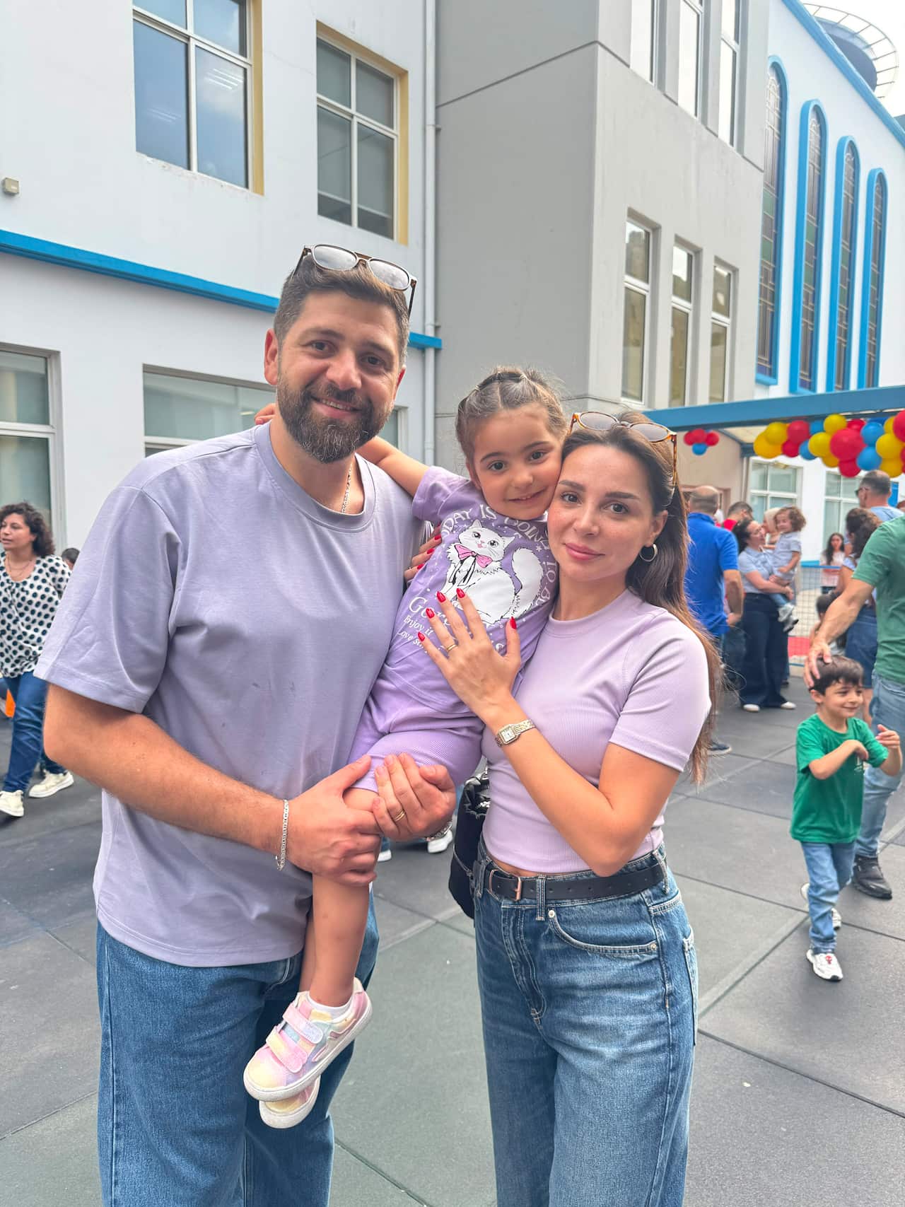 A man, woman and child, all wearing purple shirts, standing outdoor near buildings.