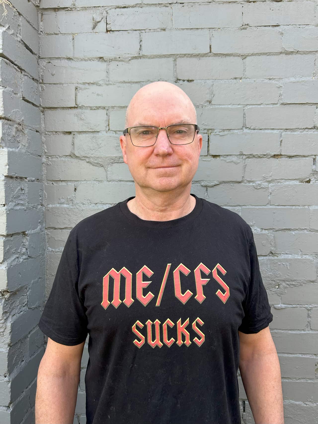 A man in black T-shirt with the words 'ME/CFS sucks' written on the front.