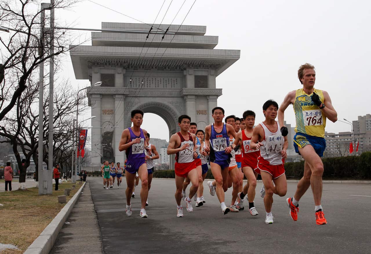 A group of runners heading down a path away from an archway monument.