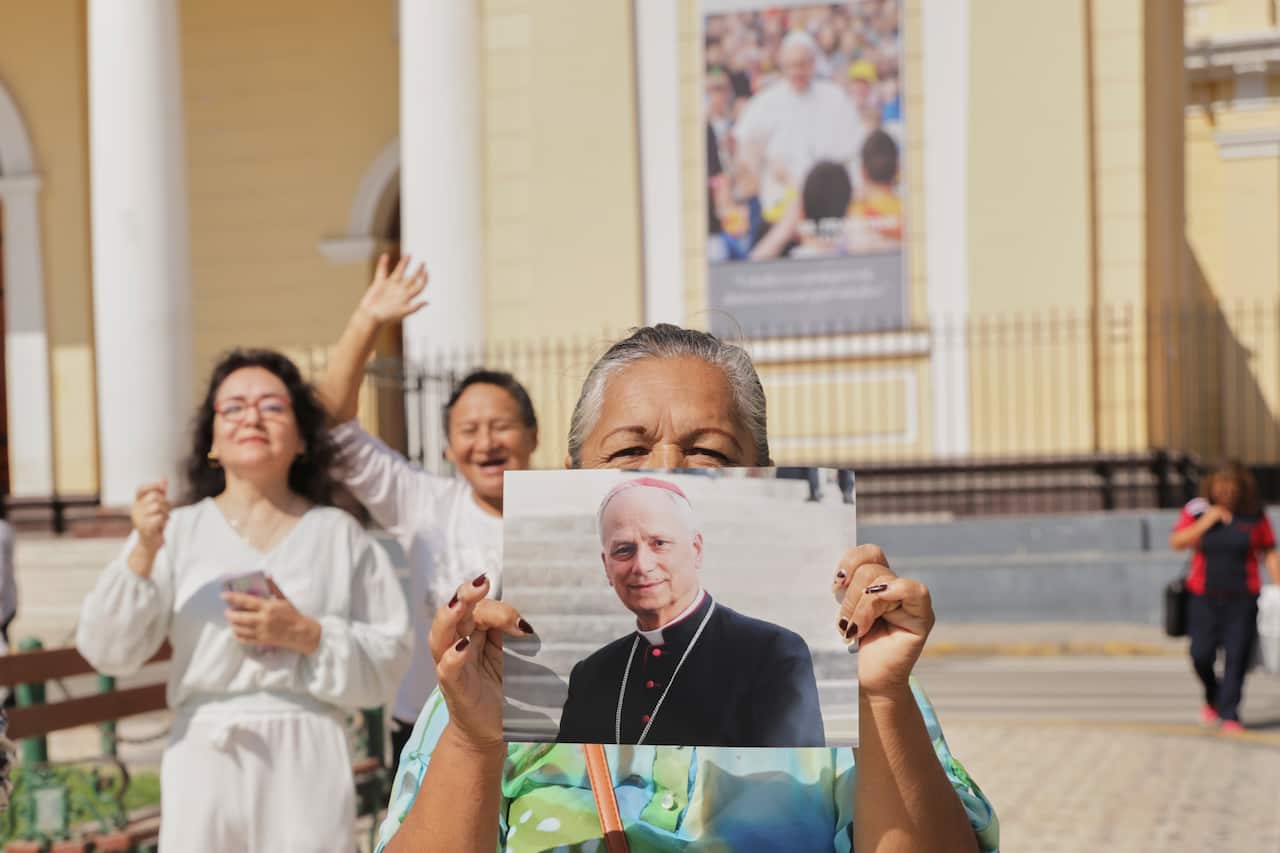A woman holds a photo of Bishop Robert Prevost as two women behind her stand with jubilant expressions.