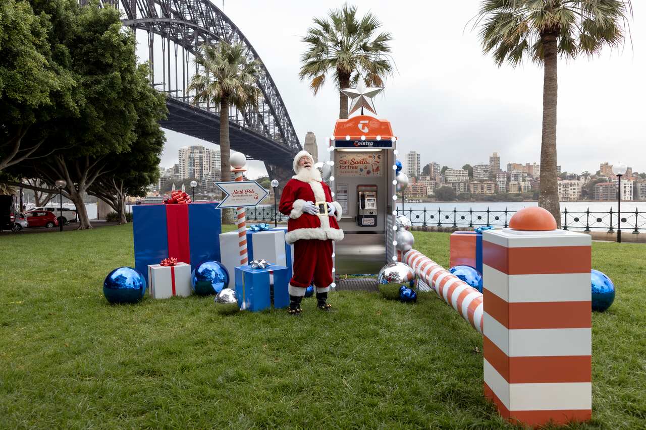 Santa standing in front of a payphone near the Sydney Harbour Bridge
