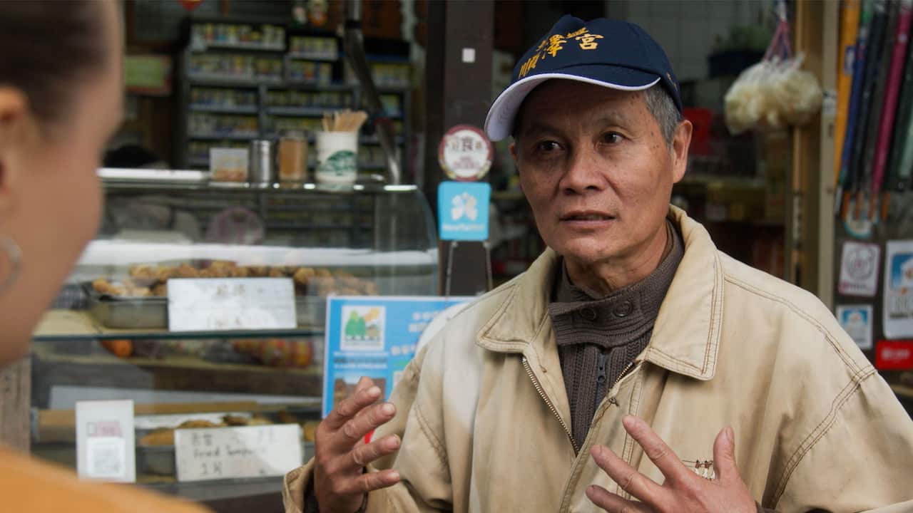 An elderly Asian man wearing a beige jacket and a blue baseball cap