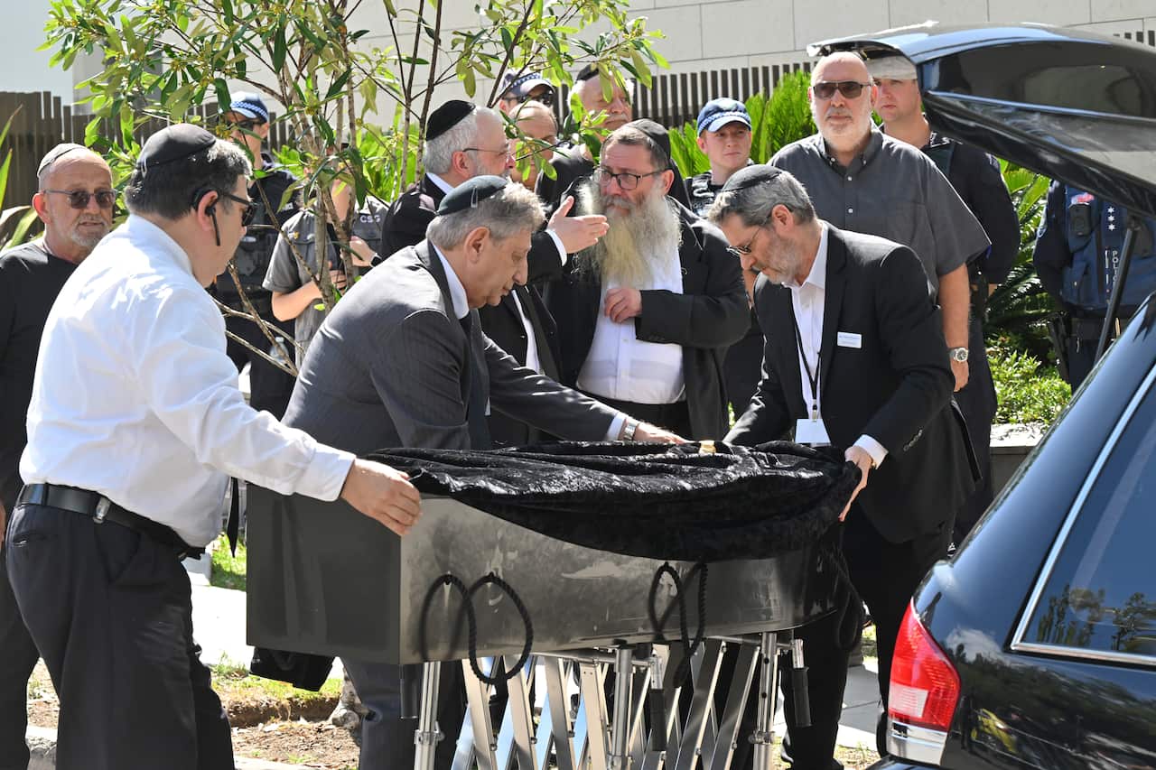 Men wearing black suits carry a black coffin. 