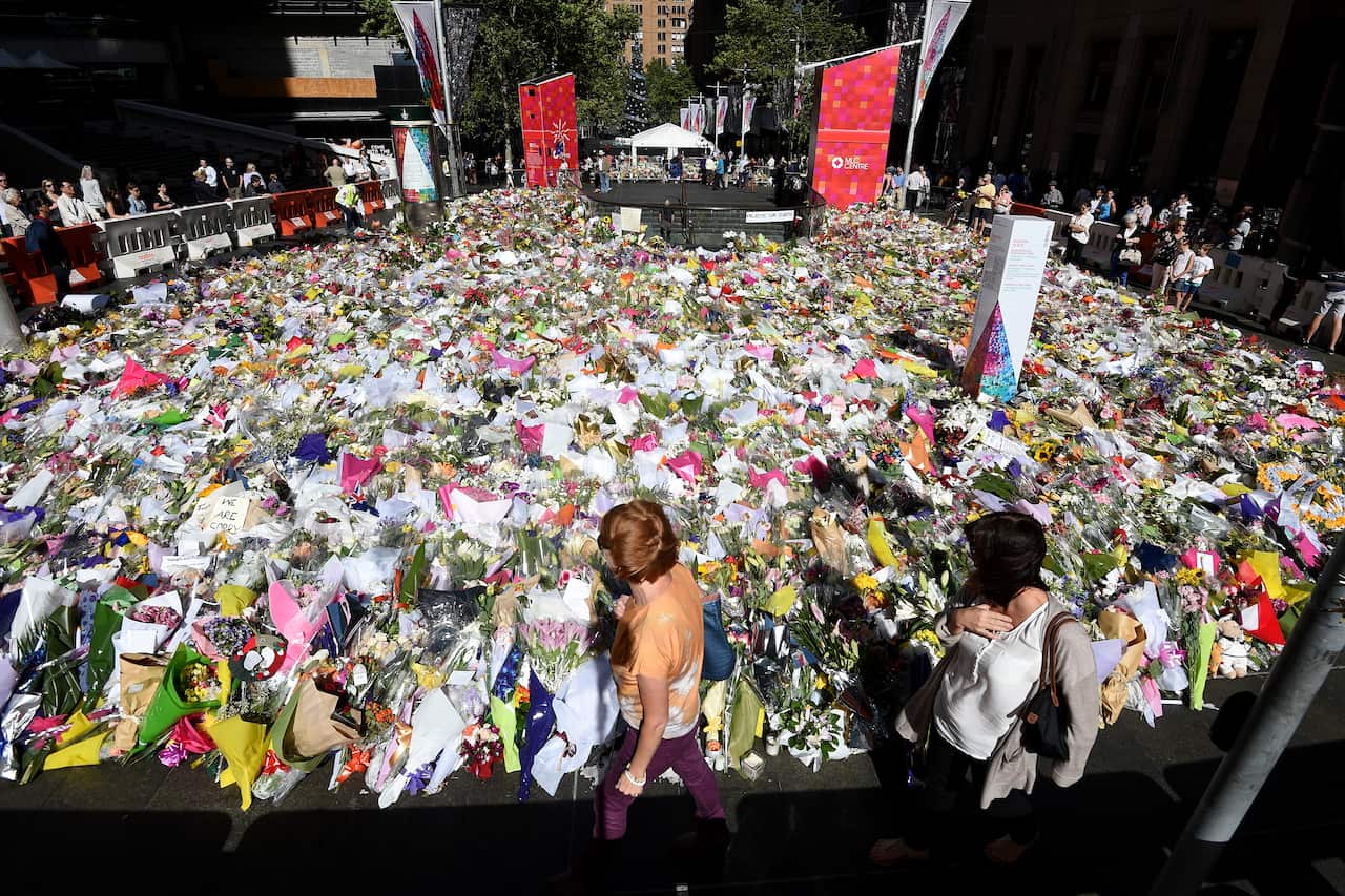 A small group of people walk past a large mass of flower bouquets laying on the street