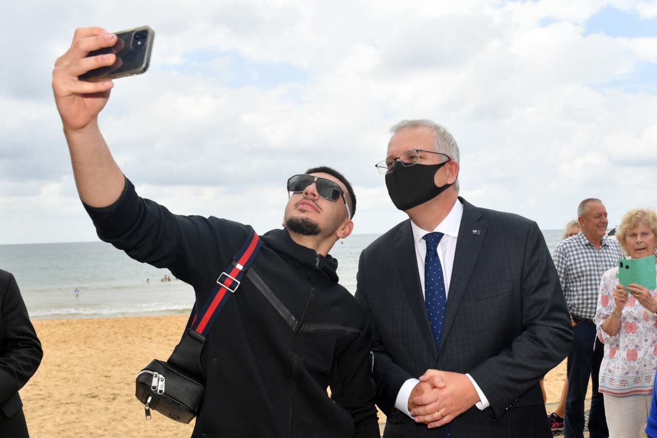 Scott Morrison poses for a selfie with another man while standing on the beach
