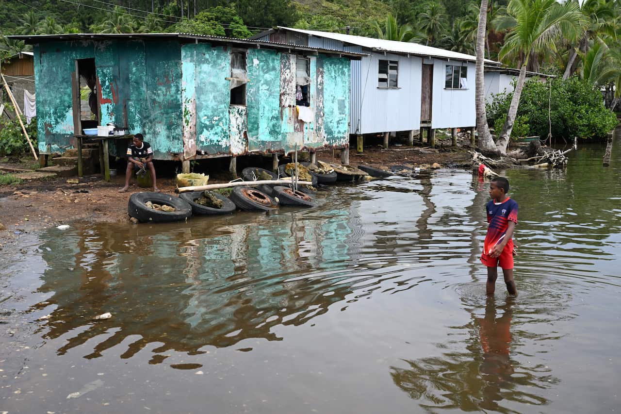 A young child standing in rising water level outside a house